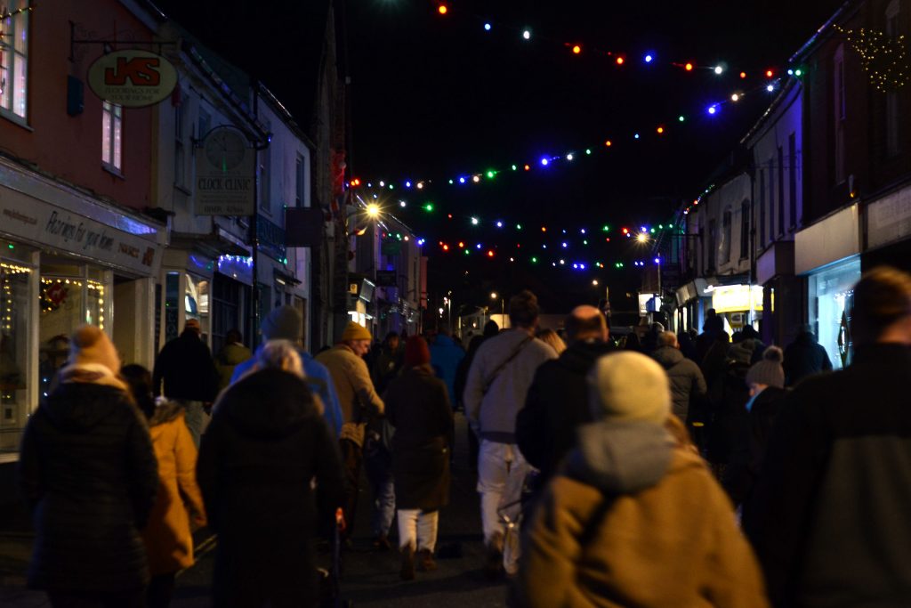 A group of carnival visitors walking up New Street in Honiton in the dark with Christmas lights above them