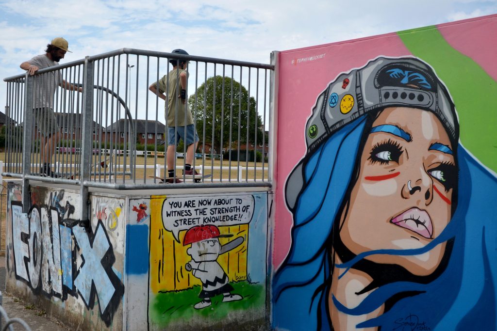 The Honiton skate park with the new skater girl mural and two skateboarders at the top of the ramp